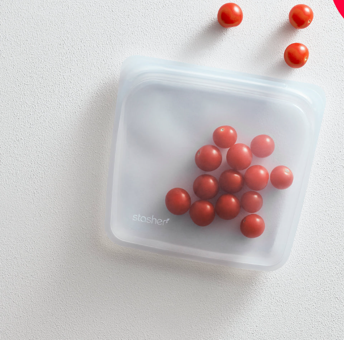Clear silicone sandwich bag with a label, containing small red tomatoes, placed on a white surface.