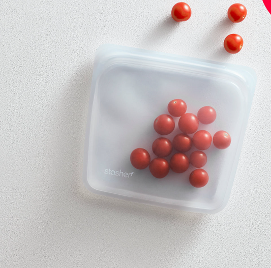 Clear silicone sandwich bag with a label, containing small red tomatoes, placed on a white surface.