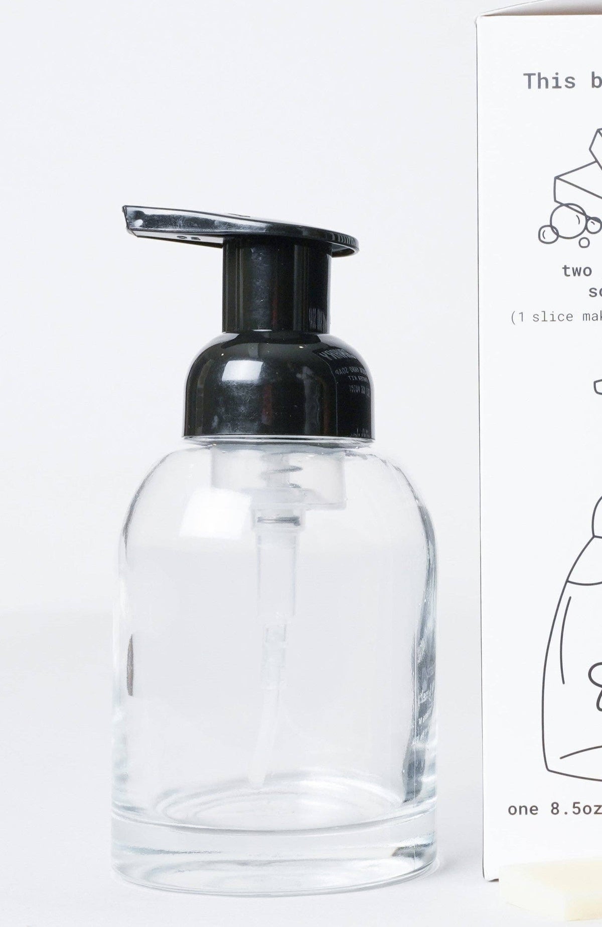 Clear glass bottle with black pump dispenser next to a box on a white background