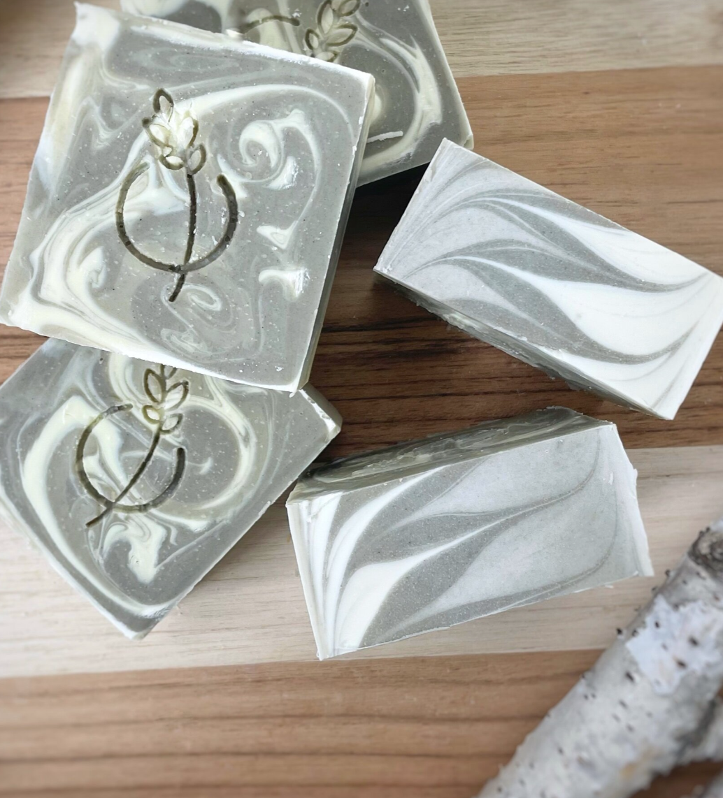 Three bars of soap with a light beige color and speckled with plant material, displayed against a marble background.