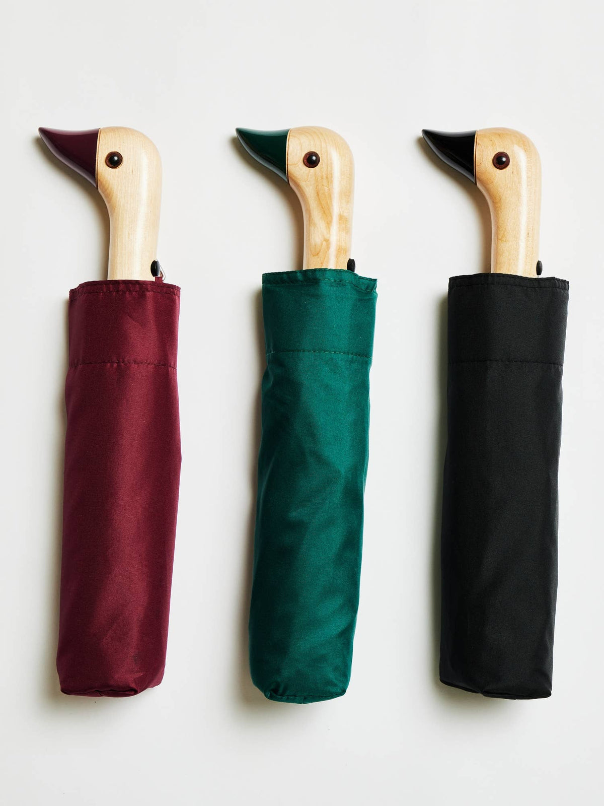 Three closed umbrellas in red, green, and black colors, with duckhead-shaped handles.