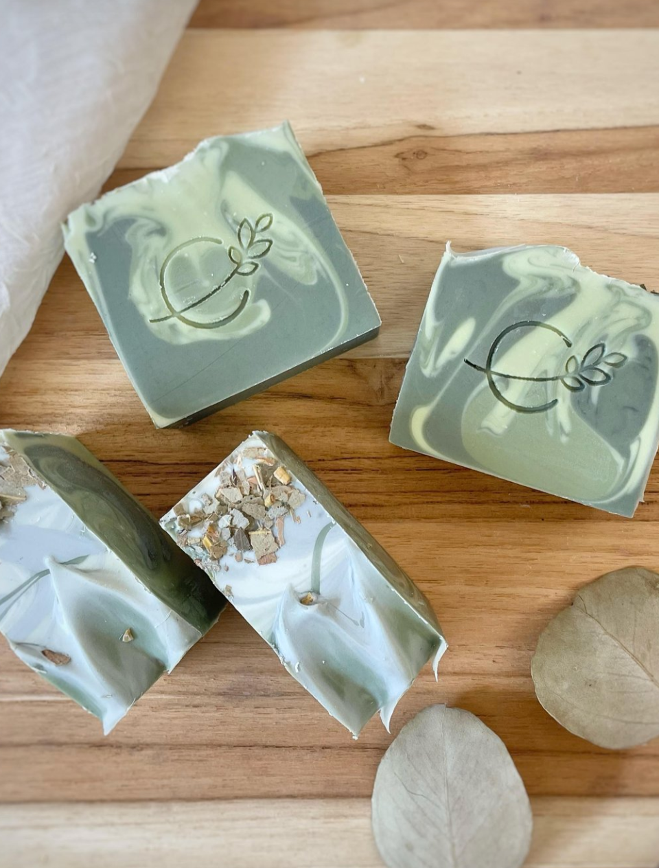 Three bars of soap with a light beige color and speckled with plant material, displayed against a marble background.
