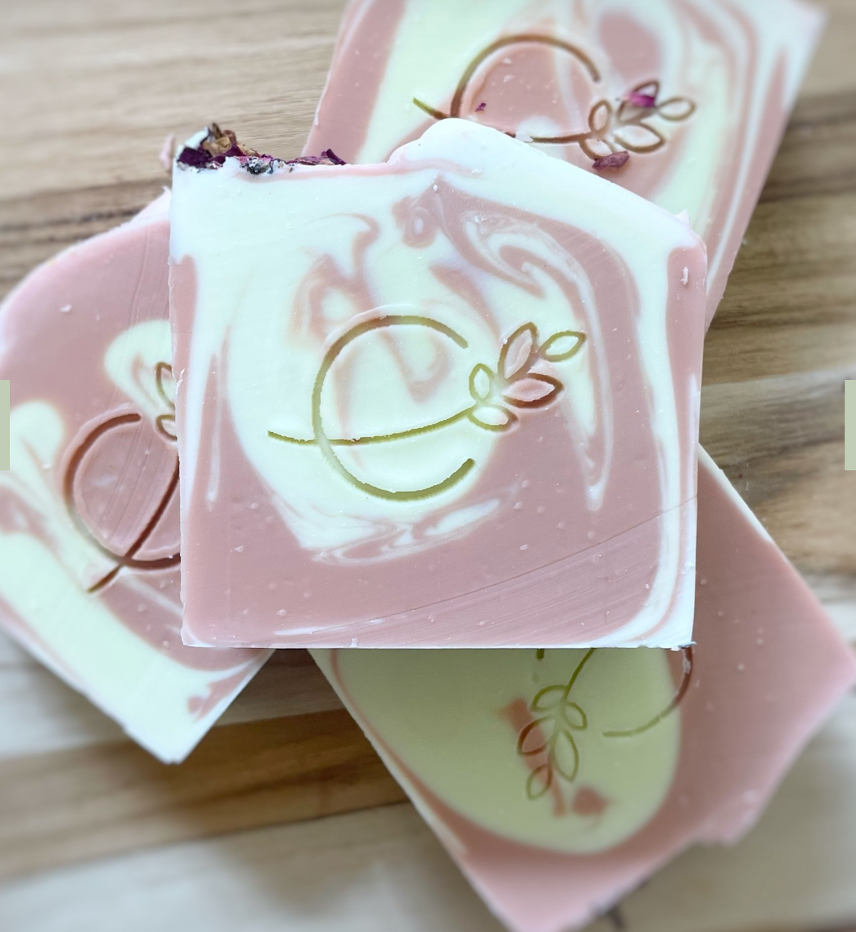 Three bars of soap with a light beige color and speckled with plant material, displayed against a marble background.
