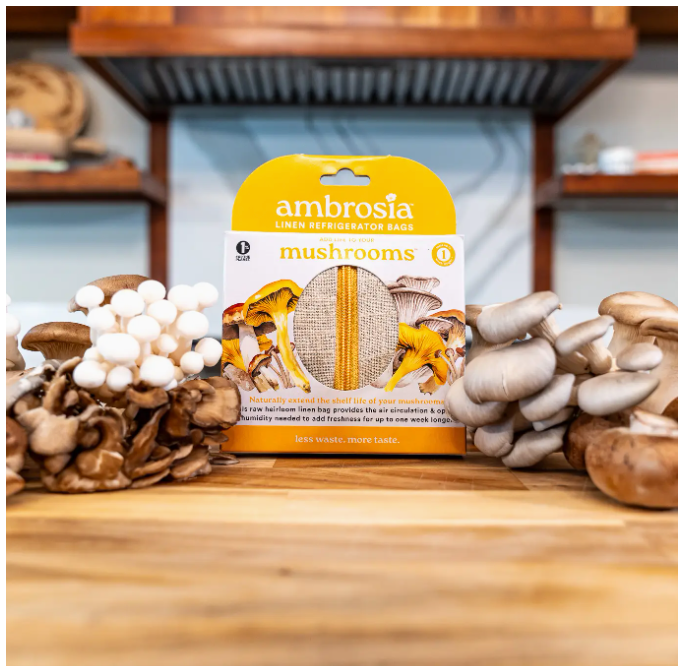 Ambrosia mushroom packaging on a wooden surface with various types of mushrooms around.
