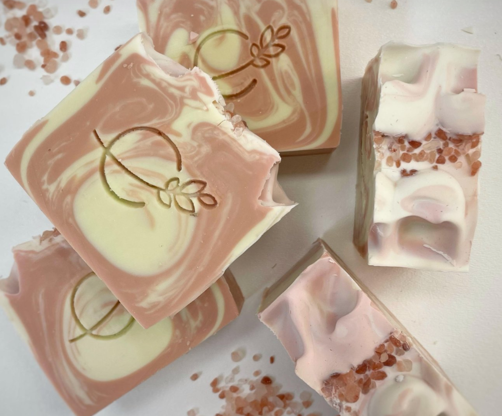 Three bars of soap with a light beige color and speckled with plant material, displayed against a marble background.