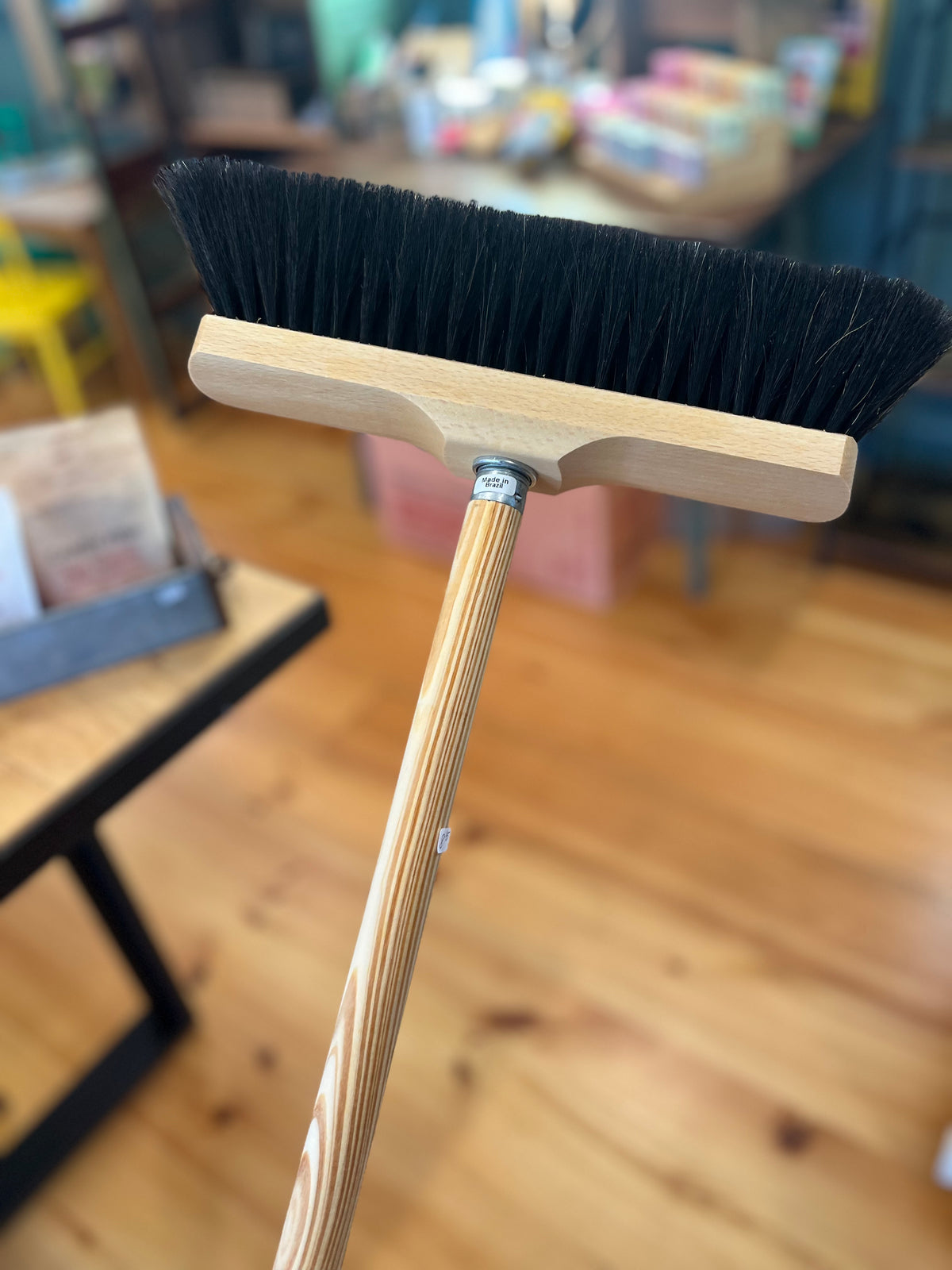Broom with wooden handle and black bristles on a blurred indoor background