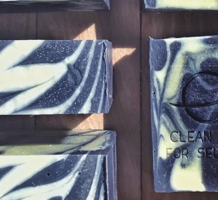 Three bars of soap with a light beige color and speckled with plant material, displayed against a marble background.